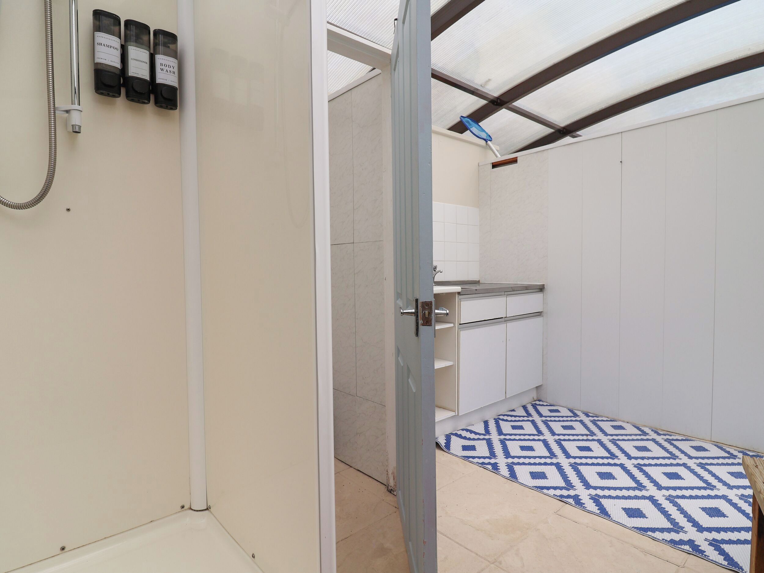 Un baño con ducha, inodoro y lavamanos. Hay tres botellas de champú, acondicionador y gel de baño en la pared.