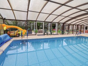 Une piscine couverte avec un toboggan, des chaises et un espace patio.