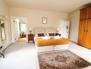Un dormitorio con cama, mesitas de noche, armario, alfombra y una puerta que da a otra habitación.