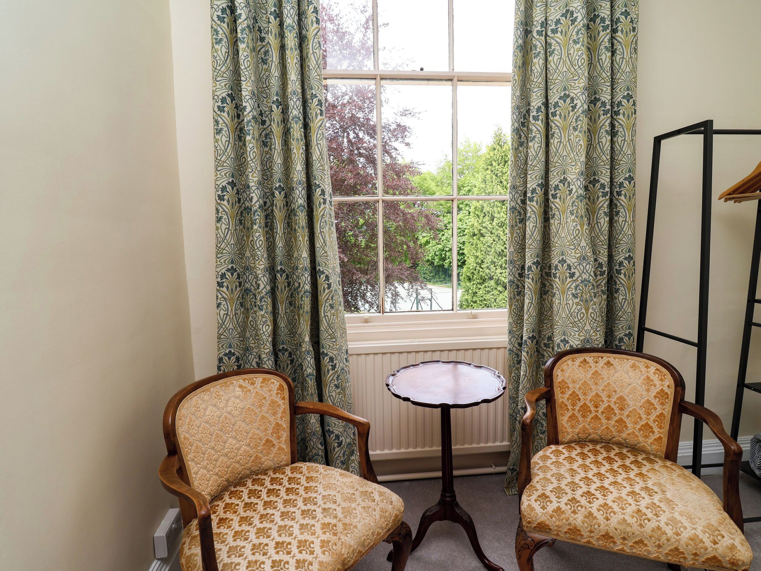 A room with two patterned chairs, a small round table, and a window with curtains.