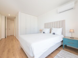 A bedroom with a bed, bedside tables, an air conditioning unit, and a hallway leading to a closet. - OL RETREAT 4 2.AE in Olhão (Olhão)