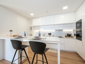 A modern kitchen with white cabinetry, two black bar stools, and a central island with a sink and countertop. - OL RETREAT 4 2.AE in Olhão (Olhão)