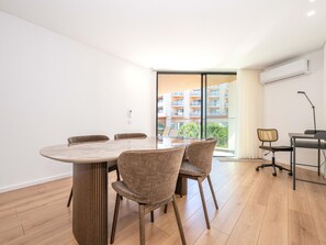 A modern room with a round table, four chairs, a desk with a chair, and a large window with a view of buildings. - OL RETREAT 4 2.AE in Olhão (Olhão)
