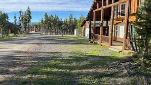 A log cabin with a porch, surrounded by trees and a gravel path. - Cracked Noggin Lodge (Dubois)