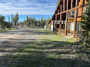 A log cabin with a porch, surrounded by trees and a gravel path.