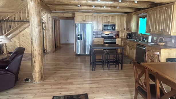 A log cabin interior with a kitchen, dining area, and a staircase. - Cracked Noggin Lodge (Dubois)