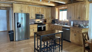 A kitchen with wooden cabinets, stainless steel appliances, and a wooden dining table. - Cracked Noggin Lodge (Dubois)