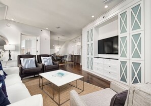 Ein modernes Wohnzimmer mit einem weißen Sofa, einem Couchtisch und einem an einem weißen Schrank mit Glasverkleidung angebrachten Fernseher.