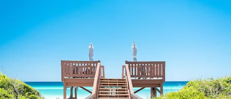 A wooden staircase leading to beach chairs overlooking a clear blue ocean.