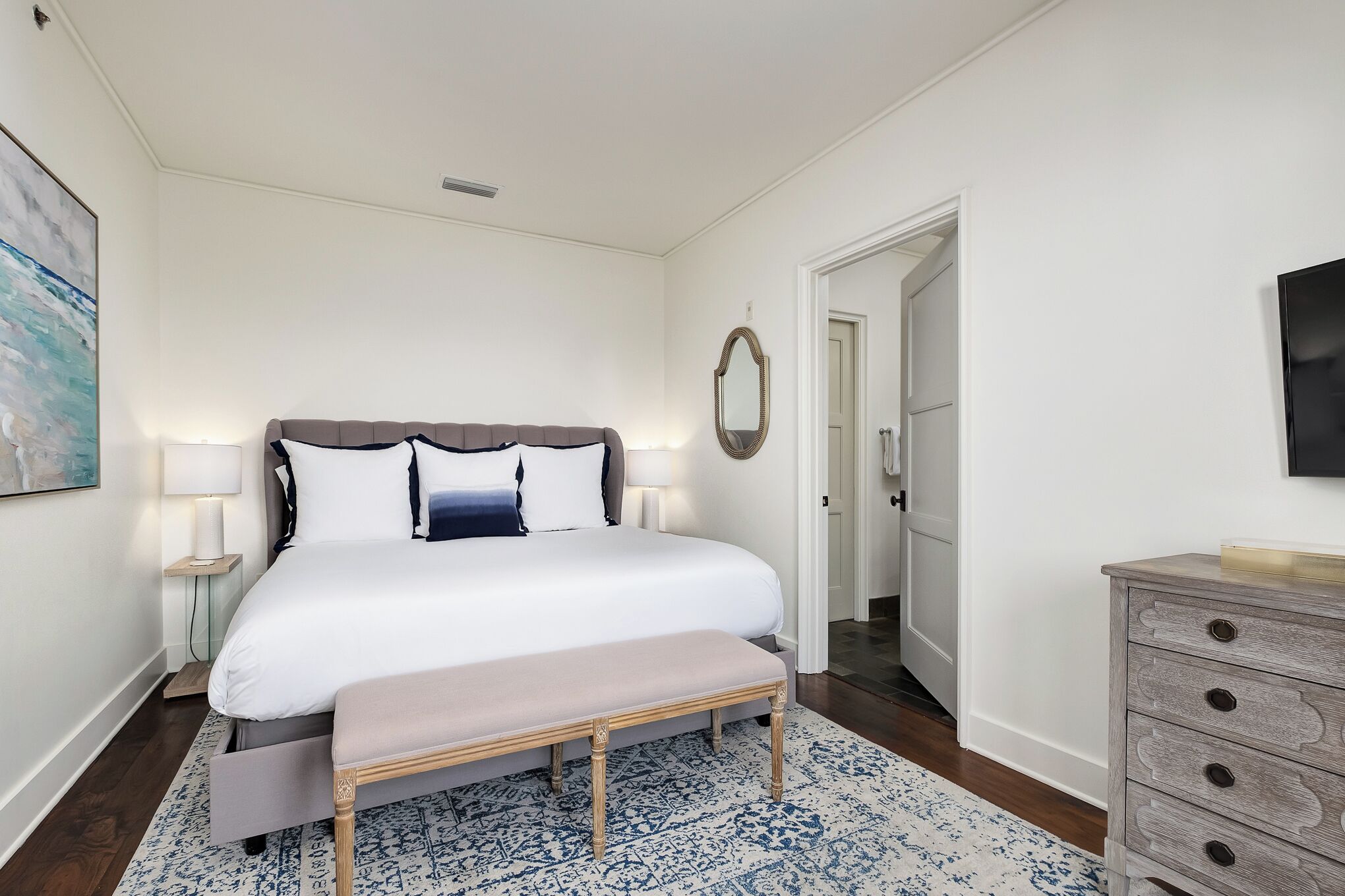Ein Schlafzimmer mit einem großen Bett, Nachttischlampen, einer Bank, einem Schminktisch und einem Spiegel an der Wand.