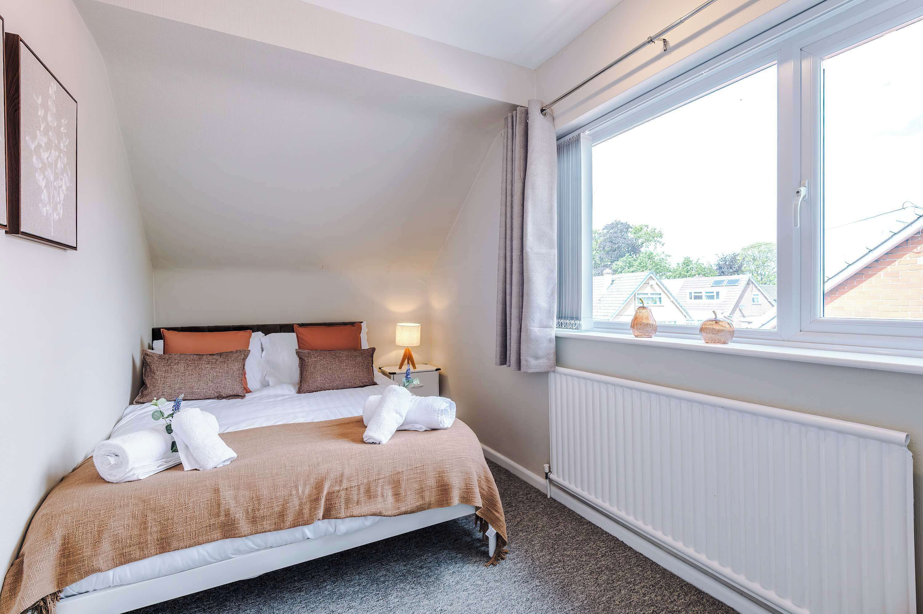 A neatly made bed with a headboard, a bedside table with a lamp, and a window with curtains.