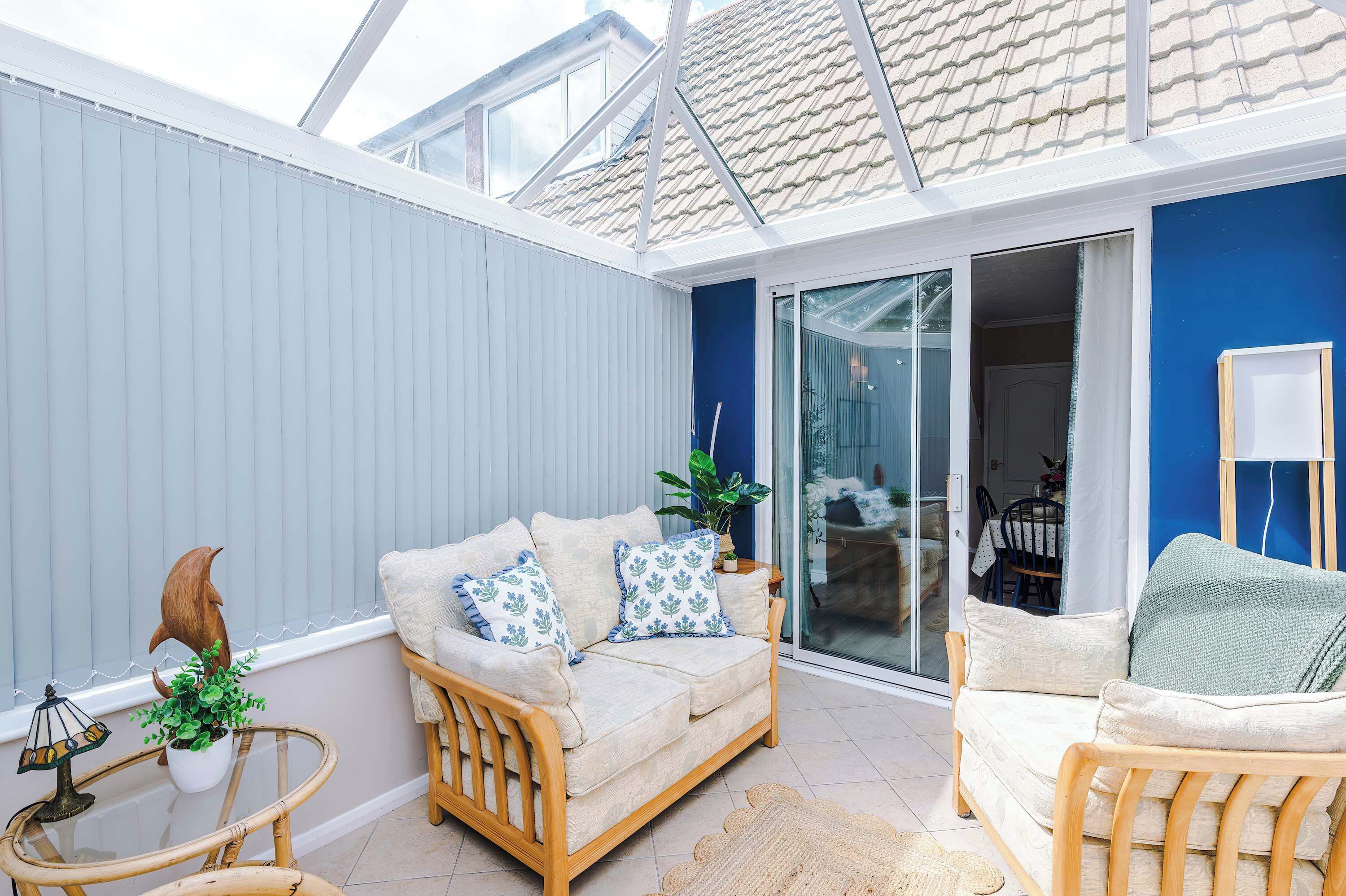 En solbeskinnet terrasse med en hvid sofa, en træstol og en glasdør, der fører til et spiseområde indendørs.