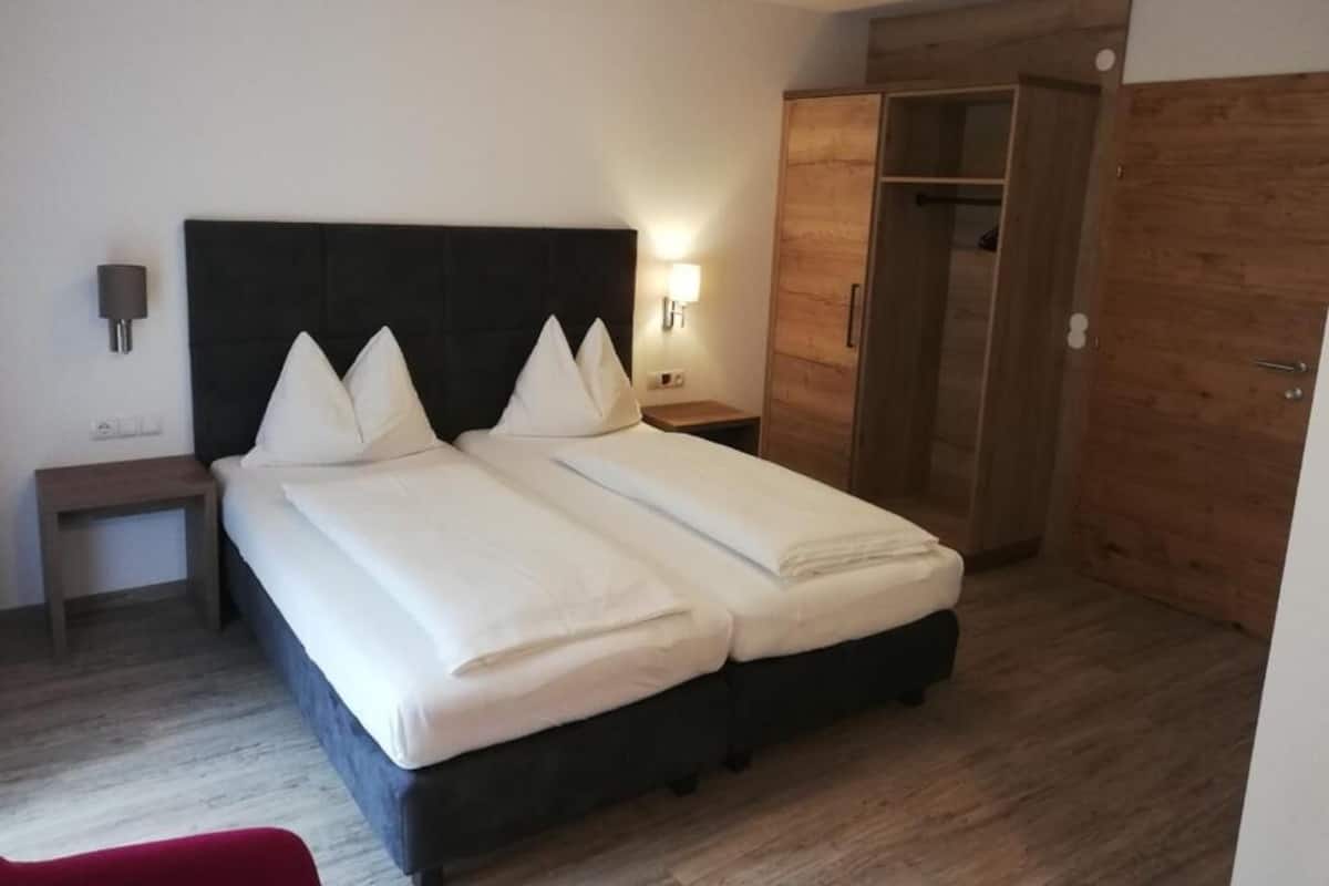 A double bed with a black headboard, a wooden wardrobe, and a nightstand with a lamp.