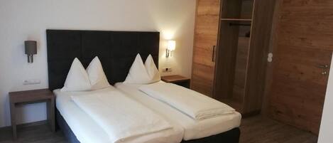 Una cama doble con cabecera negra, un armario de madera y una mesita de noche con lámpara.