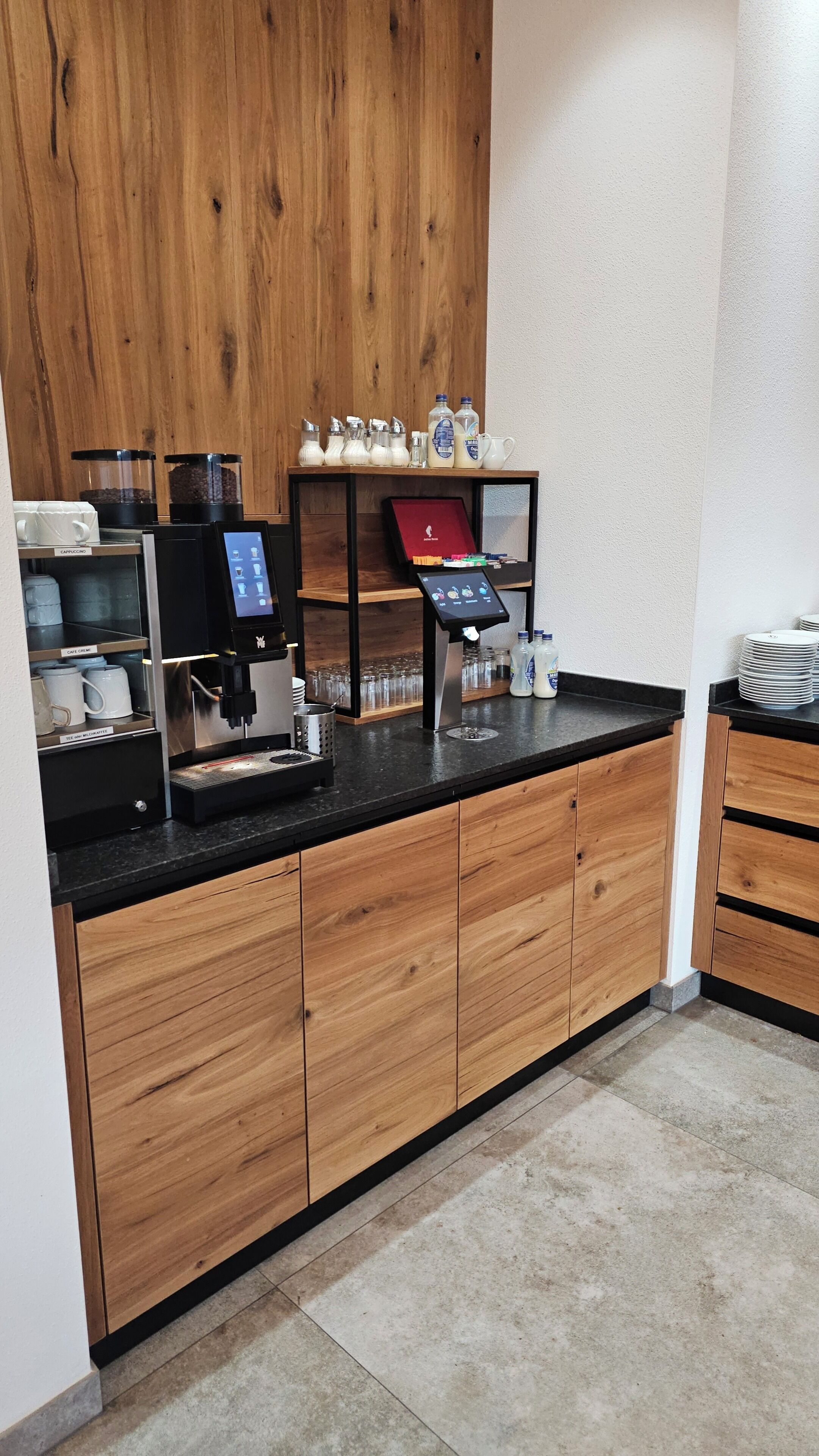 Una estación de café con una máquina expendedora, dispensadores de leche y una variedad de tazas y vasos.