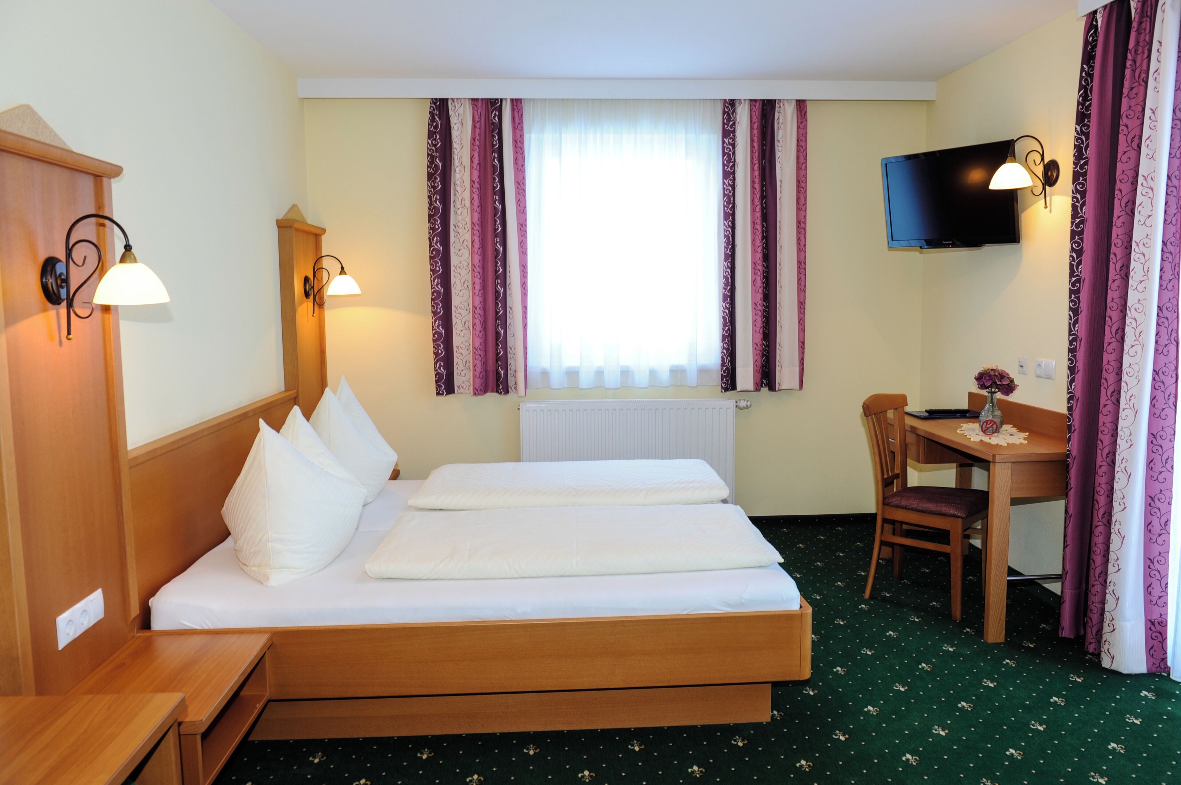 A hotel room with a bed, a desk, a chair, a television, and curtains.