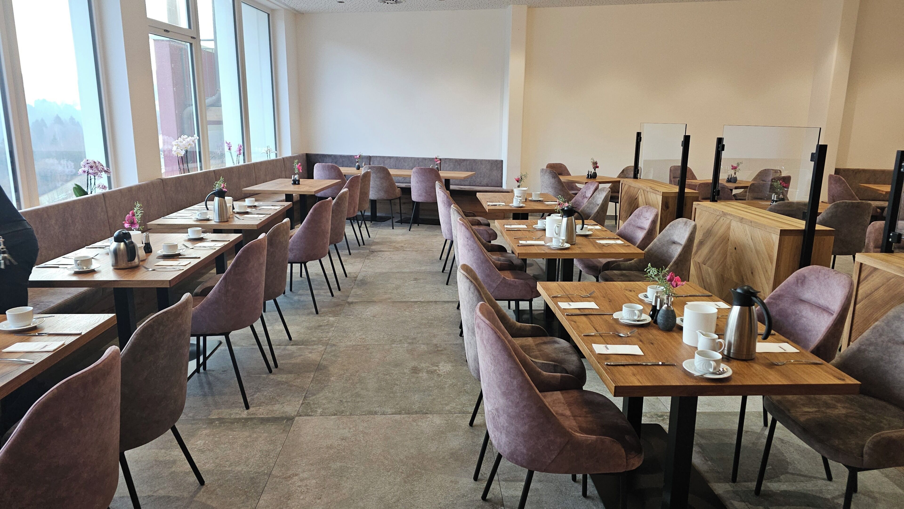 A spacious dining area with multiple tables and chairs, large windows, and a neutral color scheme.