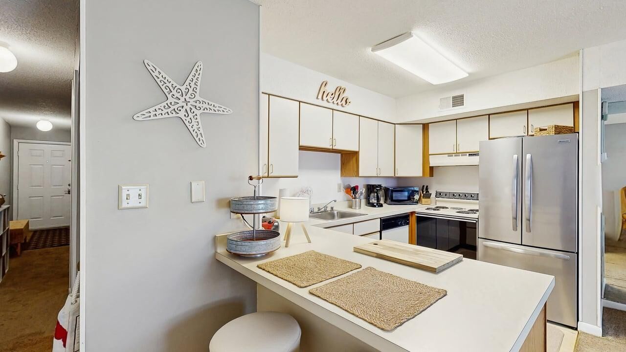 A modern kitchen with white cabinetry, a stainless steel refrigerator, a microwave, and a coffee maker.