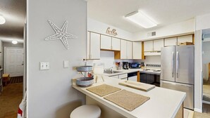 Een moderne keuken met witte kastjes, een roestvrijstalen koelkast, een magnetron en een koffiezetapparaat.