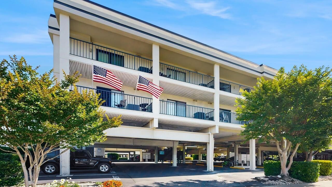 Ein mehrstöckiges Hotel mit amerikanischen Flaggen, einem überdachten Parkbereich und einem begrünten Eingangsbereich.