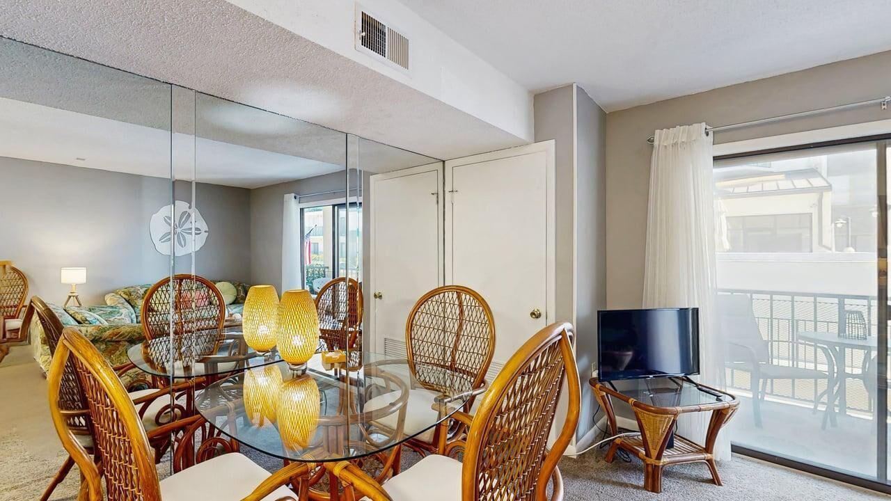 Ein Hotelzimmer mit einem Glastisch, Korbstühlen, einem Flachbildfernseher, einem Balkon mit Aussicht und einer Schiebetür aus Glas.
