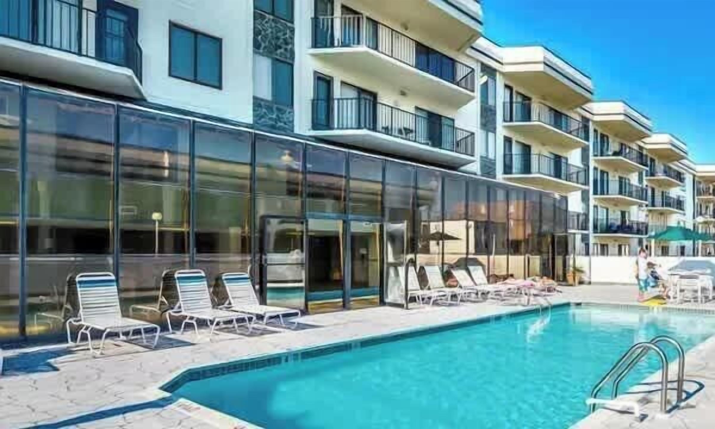 Et moderne hotel med swimmingpool, liggestole og en balkon med glasfacade.