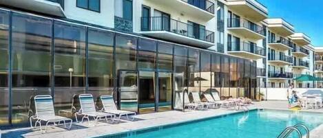 Et moderne hotel med swimmingpool, liggestole og en balkon med glasfacade.