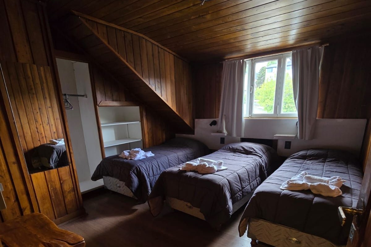 Et hyttekammer med to senge, trælofter og et vindue med gardiner.