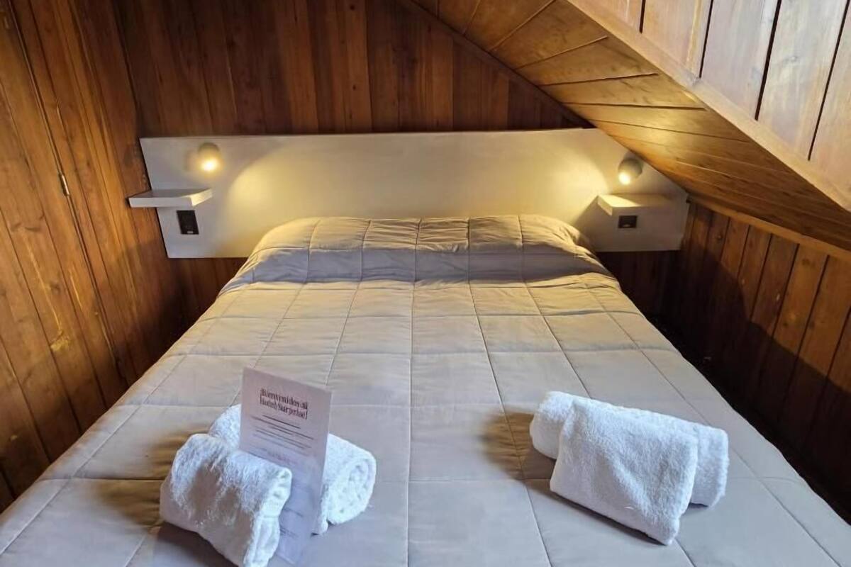 A cozy room with a bed, two towels, and a sign on the bed.