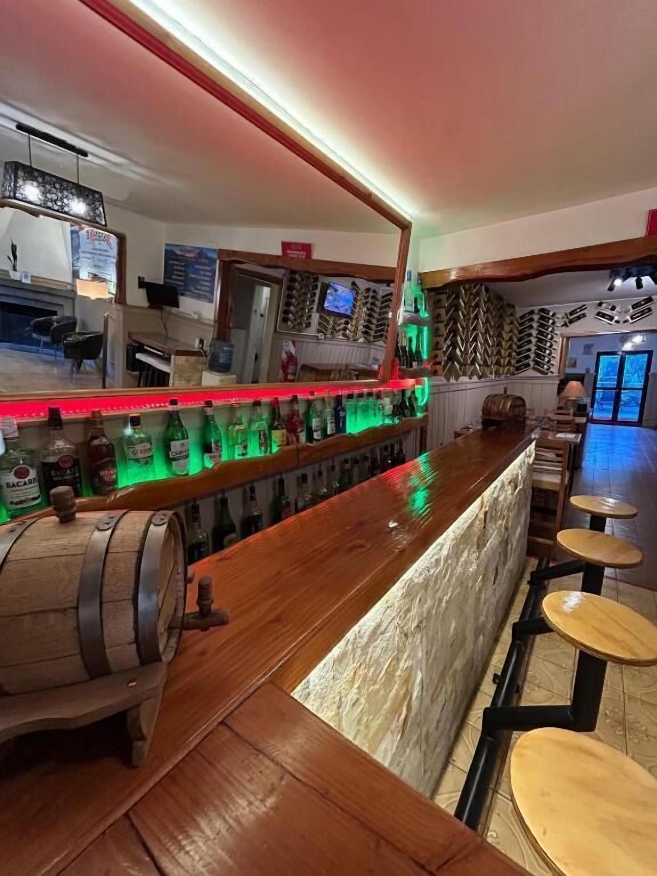 Zona de bar con mostrador de madera, taburetes y un barril de madera grande.