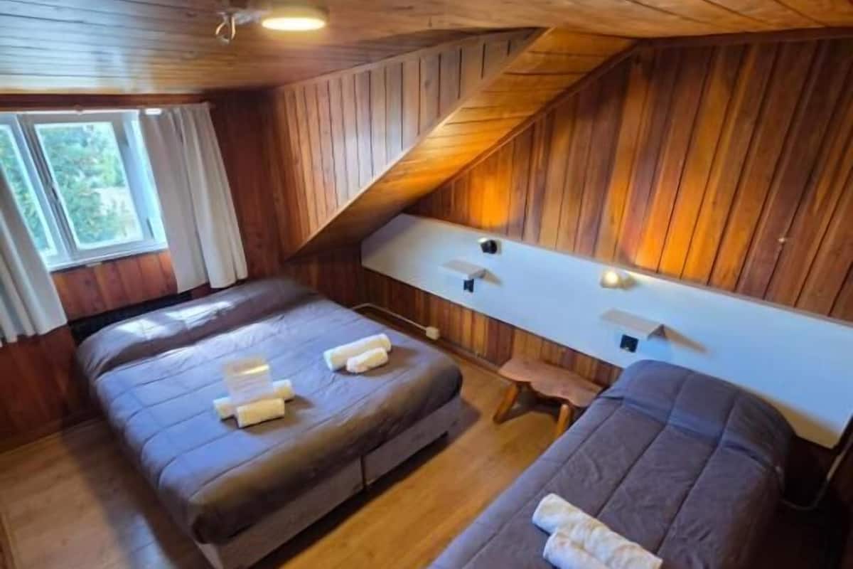 A room with two beds, a wooden ceiling, a window, and a white table.