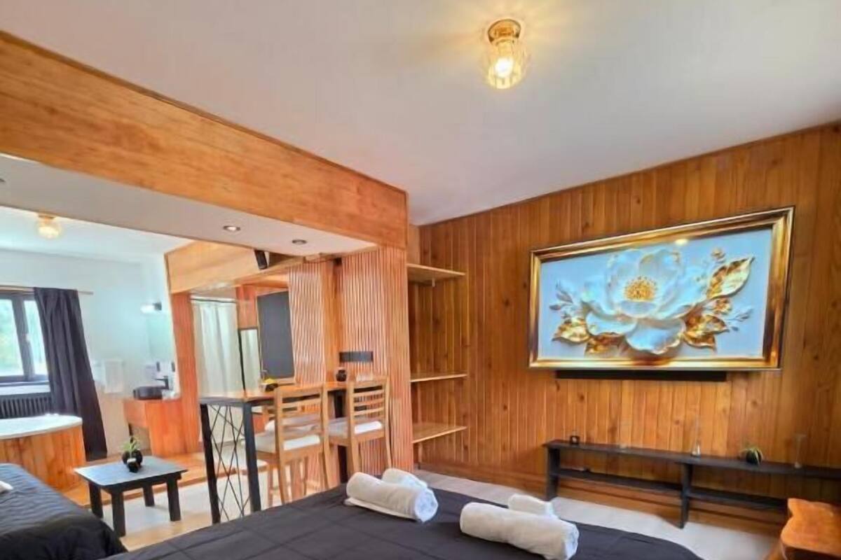 A hotel room with a large bed, a wooden headboard, a painting on the wall, and a desk with a chair.