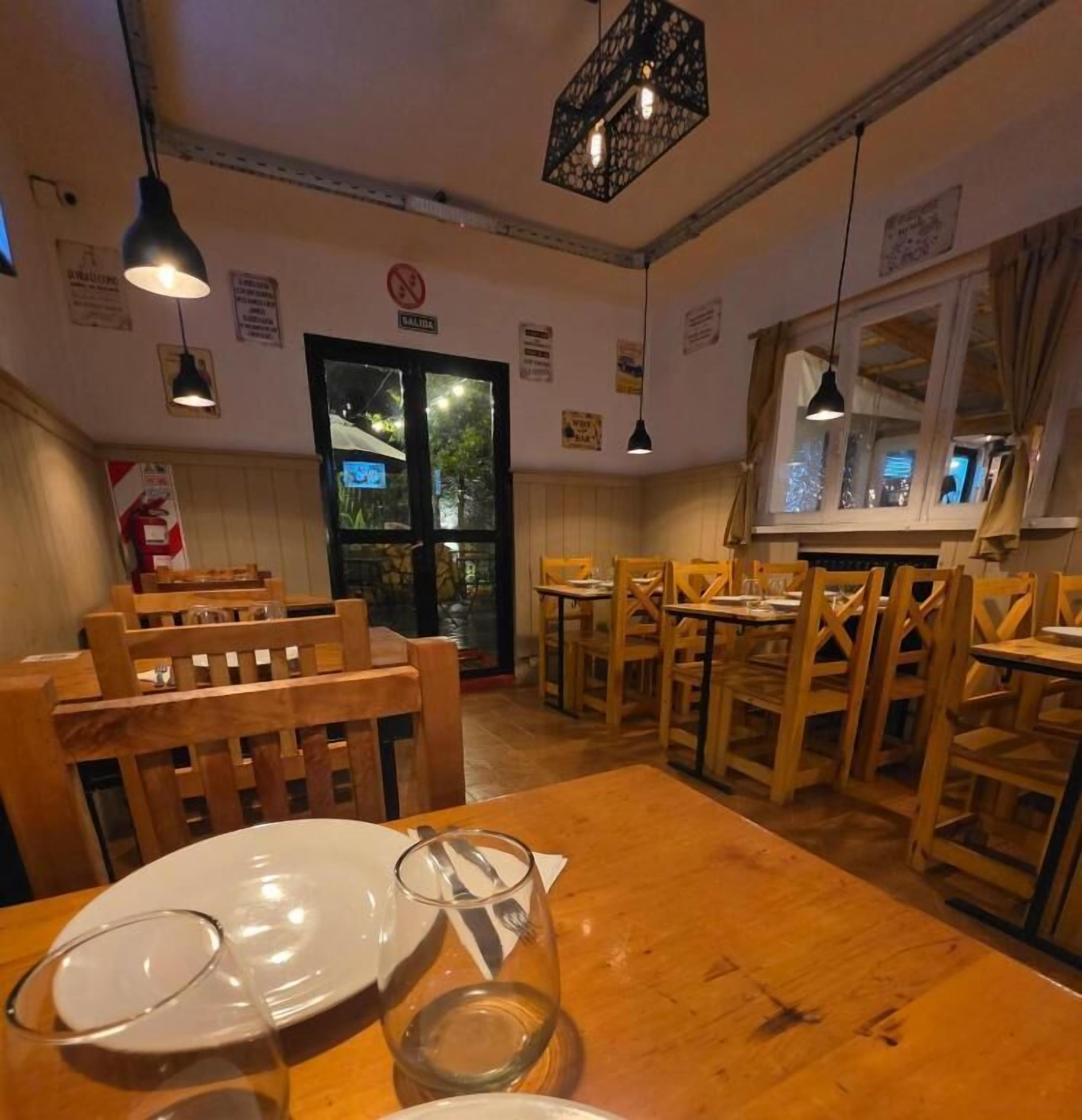 Een restaurantinterieur met houten tafels en stoelen, hangende吊灯 en een raam met uitzicht op bomen.