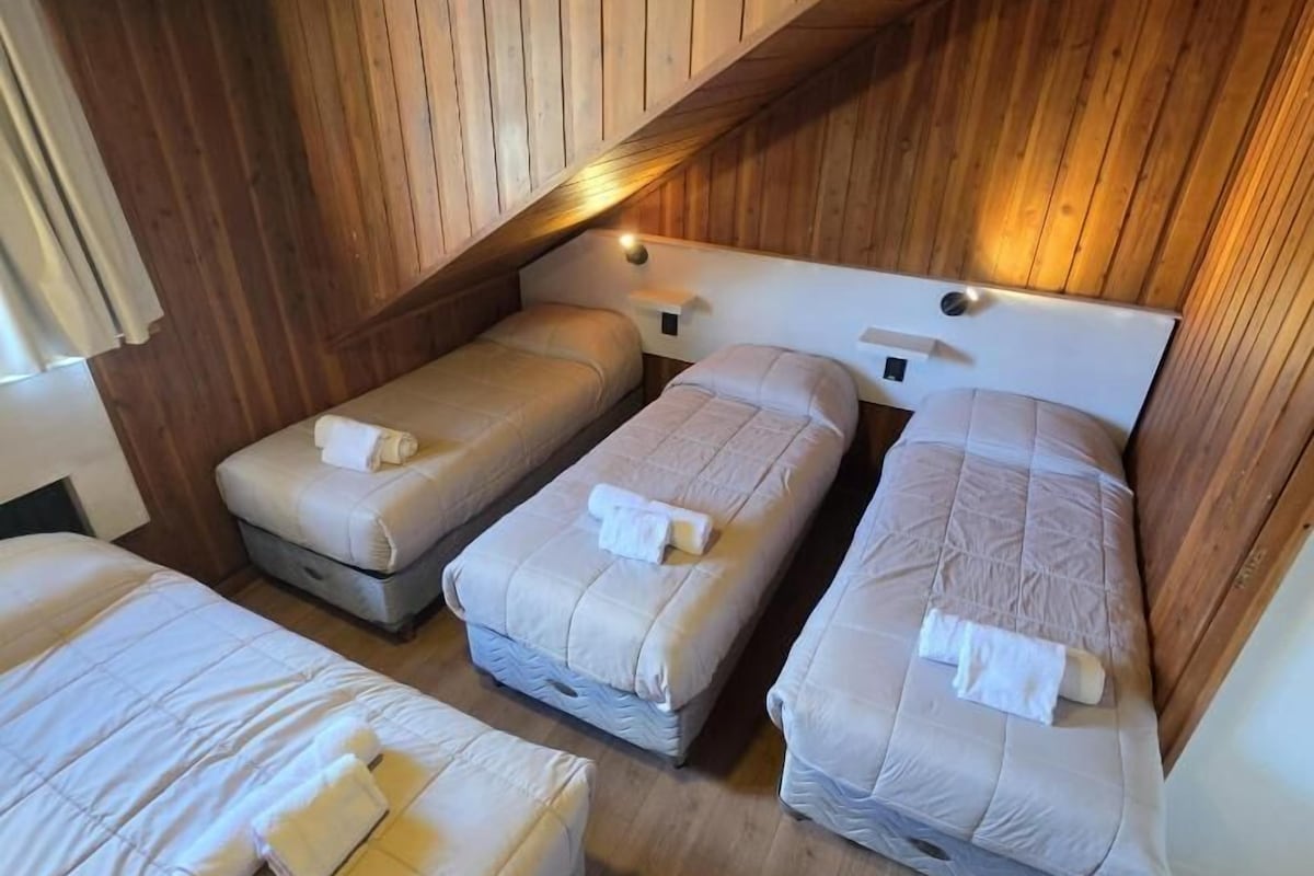 Una habitación con cuatro camas ubicadas en una esquina, paredes de madera y techo inclinado.