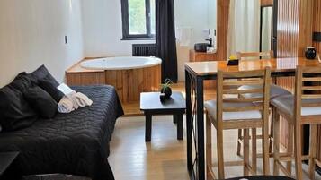 Una habitación con una cama, una mesa de comedor, sillas, una mesita con una planta y un ventanal.