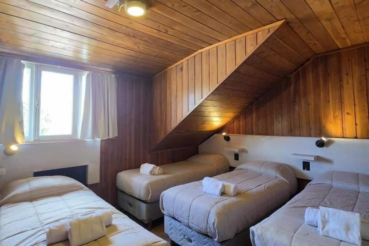 A room with three beds, wooden walls, a sloped ceiling, and a window.