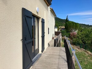 A building with a wooden deck, black shutters, and a view of a green landscape. - Maison Lara with natural swimming pool in the heart of the Cathar countryside 7 people (Saint-Ferriol)
