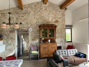 A stone-walled room with a fireplace, a wooden cabinet, a sofa, and a dining area with a table and chairs. - Maison Lara with natural swimming pool in the heart of the Cathar countryside 7 people (Saint-Ferriol)