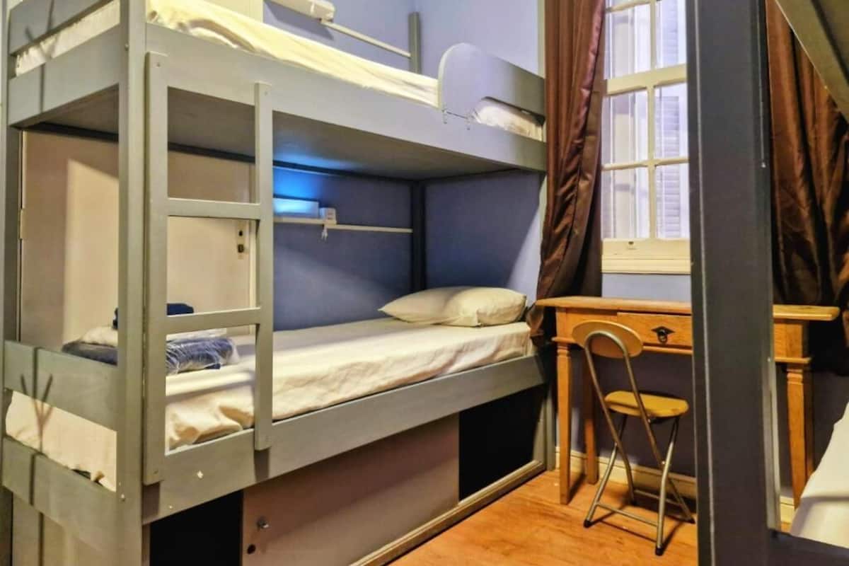 Habitación con literas, un escritorio, una silla, una ventana con cortinas y una puerta a la vista.