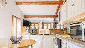 Une cuisine avec des poutres en bois, des meubles blancs, un four à micro-ondes, une machine à café et un grand four.