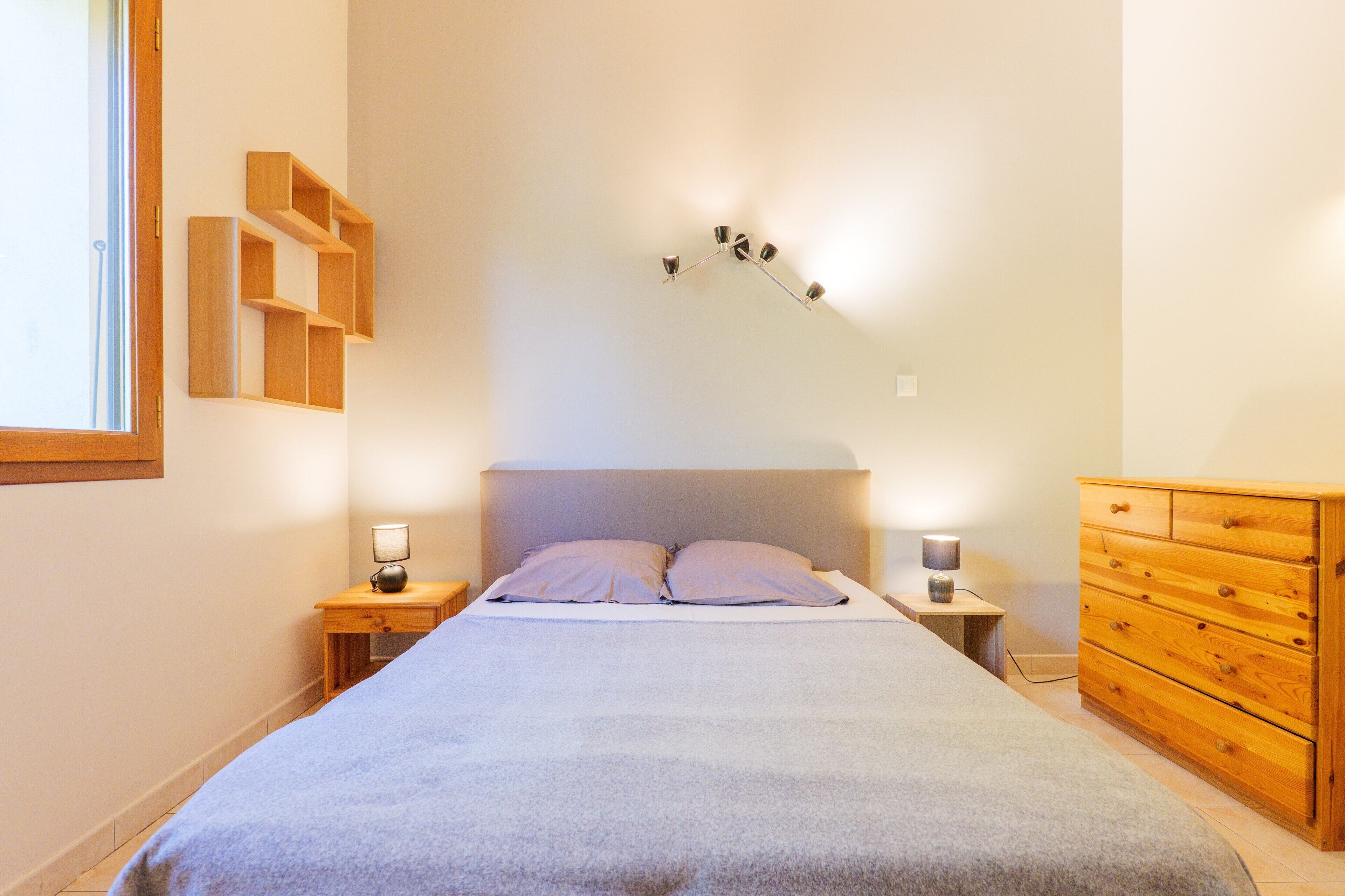Un dormitorio con cama, dos mesitas de noche, una cómoda y una lámpara de pared.
