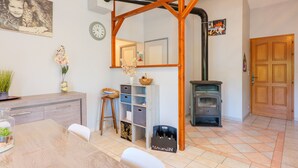 Une pièce dotée d’une structure en poutres apparentes, d’une cheminée, d’une table à manger avec des chaises, d’un petit tabouret et d’un meuble avec des tiroirs.