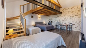 A room with two beds, a wooden staircase, a dining table with chairs, and a chandelier. - Les Carmes Guest Room: "Elisabeth" Family Room for 6 with Shared Garden & Wi-Fi (Sèvremont)