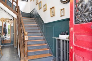 Un escalier avec des balustrades en bois et une porte rouge ornée d’un motif décoratif en forme de feuilles.