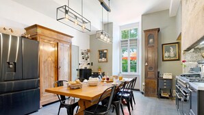 A kitchen with a wooden table, black chairs, a refrigerator, and a stove. - Les Carmes Guest Room: "Elisabeth" Family Room for 6 with Shared Garden & Wi-Fi (Sèvremont)
