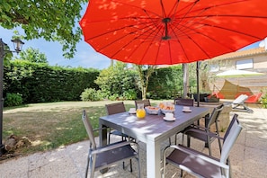 Un patio con una mesa, sillas y un paraguas rojo.