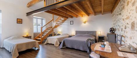 Una habitación con dos camas, una mesa de madera, una escalera y paredes de piedra.