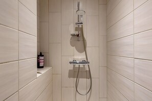 Une douche Ă©quipĂ©e dâun pommeau de douche Ă main, dâun robinet mural et dâun distributeur de savon fixĂ© sur une Ă©tagĂšre.