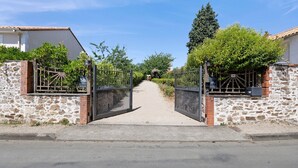 A gated entrance with a pathway leading to a building with stone walls and a tiled roof. - Les Carmes Guest Room: "Elisabeth" Family Room for 6 with Shared Garden & Wi-Fi (Sèvremont)