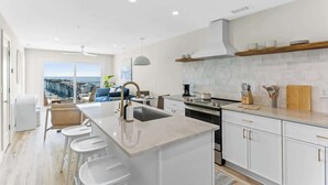 A modern kitchen with a large island, white cabinetry, and a view of the ocean. - Seaside Tranquility|North Pier Ocean Villa+Pool| (Carolina Beach)